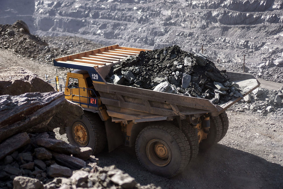 A large dump truck has a bed full of recently mined iron ore in a open pit mine