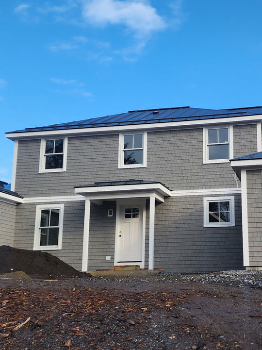 Two-story gray shingle house with white trim under construction.