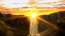 A sun setting behind a waterfall