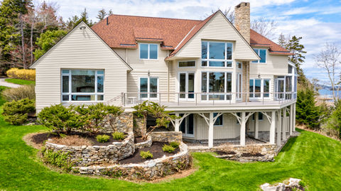 Large beige house with red roof, many windows, green lawn, ocean view.