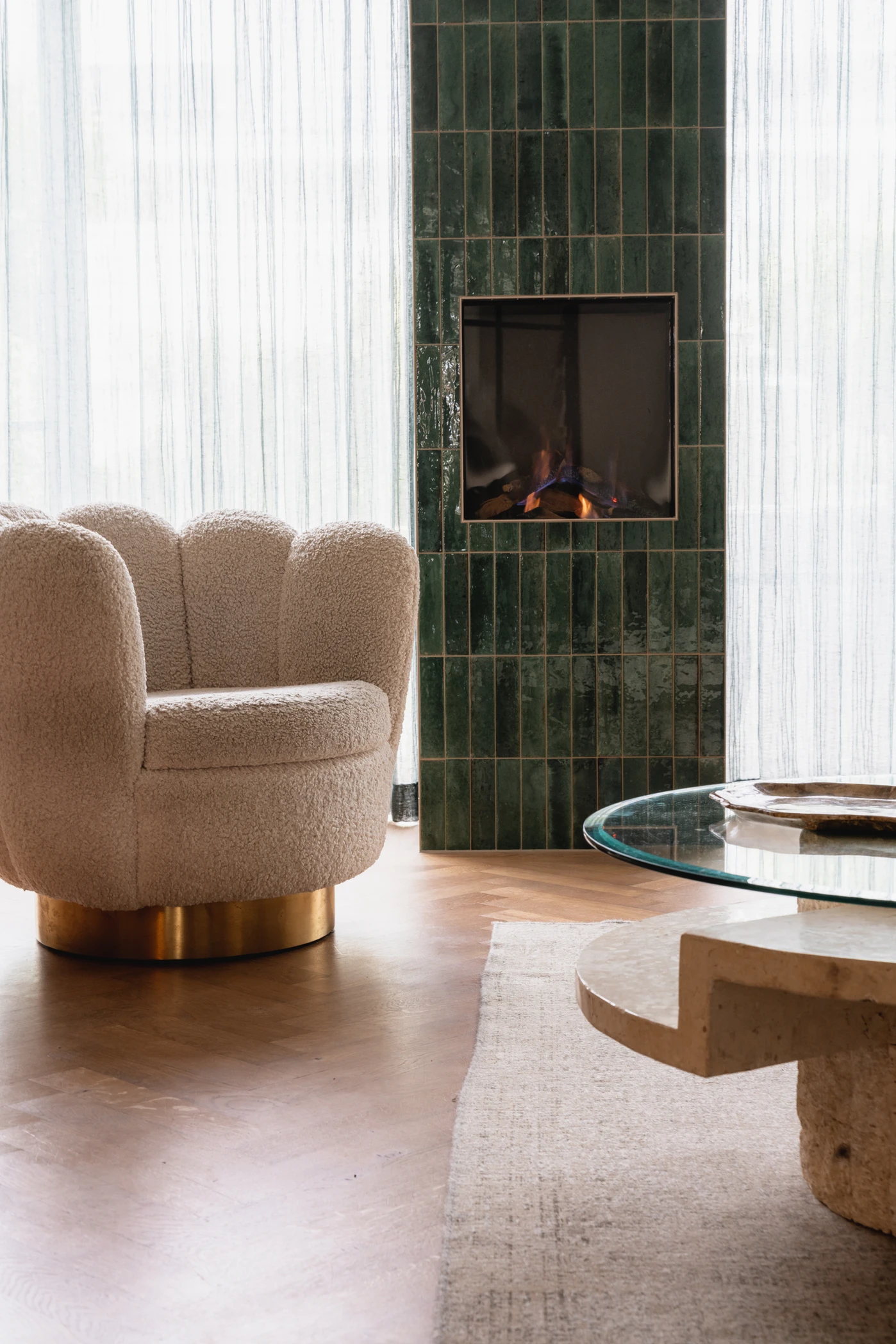 Interieurfoto van houten tafel met glazenblad met op de achtergrond een crème kleurige stoel en een haard van groene tegels