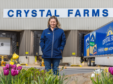 Kristi is wearing a blue jacket and is standing in front of the loading dock at the Crystal Farms production facility in the spring time.