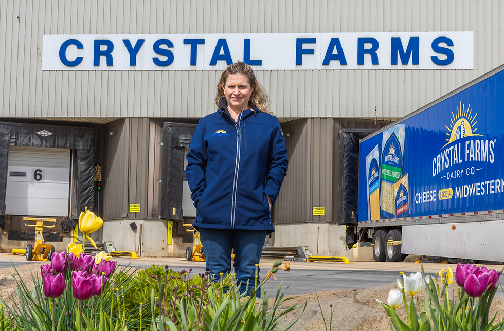 Kristi is wearing a blue jacket and is standing in front of the loading dock at the Crystal Farms production facility in the spring time.