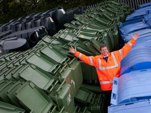 Malcom Odlin, Purchasing Manager at Luxus, standing with arms raised next to blue and green bins on Luxus site.
