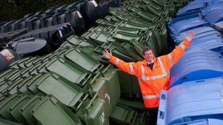 Malcom Odlin, Purchasing Manager at Luxus, standing with arms raised next to blue and green bins on Luxus site.