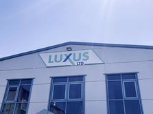 Front view of a Luxus Ltd building with the company logo displayed on the upper facade, set against a clear blue sky.
