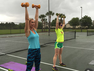 Two women performing an overhead press side by side on tennis court