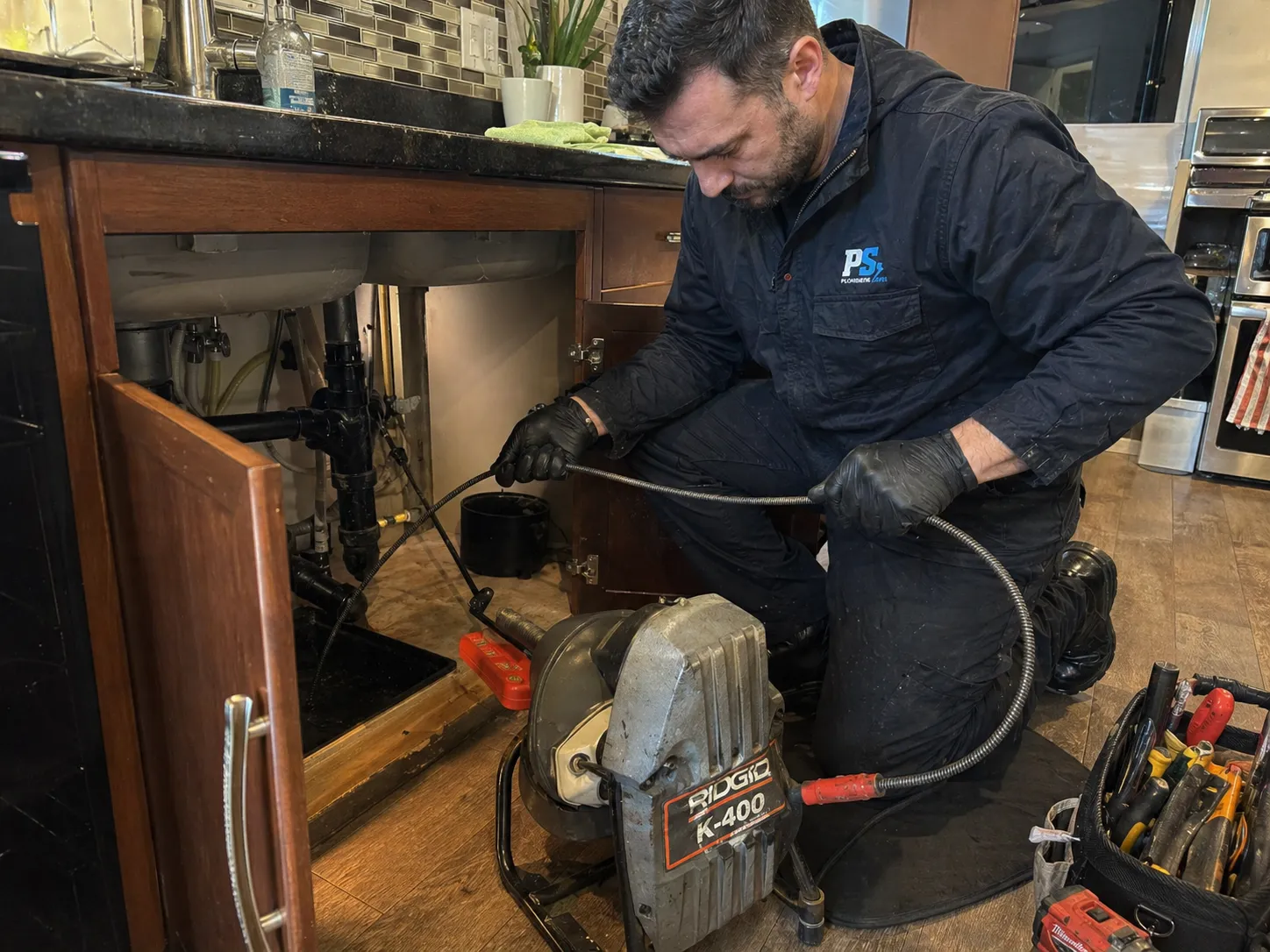 Plombier professionnel sous un évier de cuisine, utilisant une déboucheuse motorisée pour dégager la canalisation.