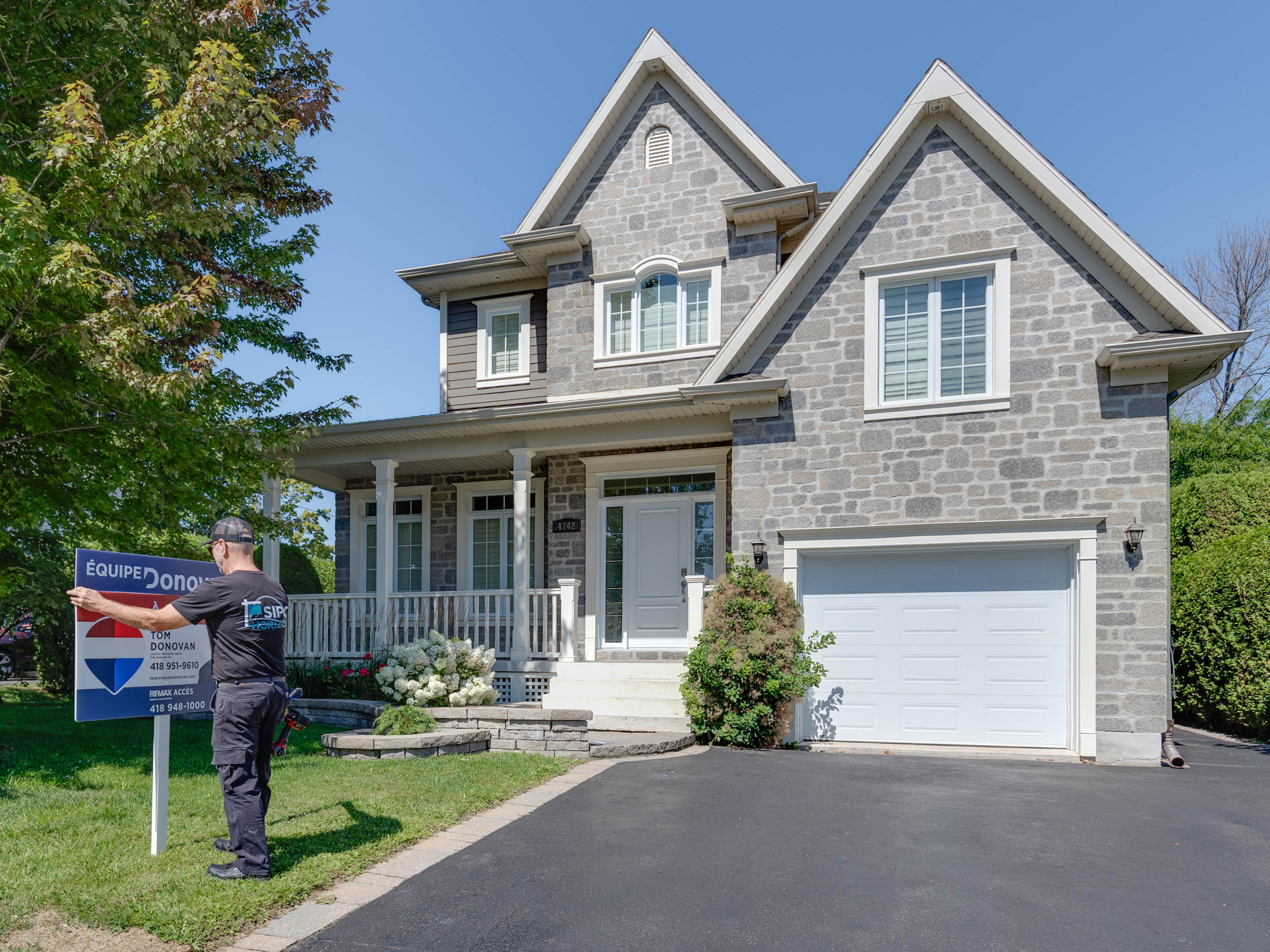 Technicien installant une pancarte immobilière devant une maison à Québec