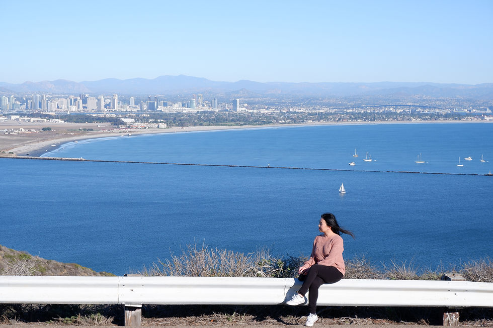 Girl sitting on a ledge and looking at the ocean view and San Diego cityscape.