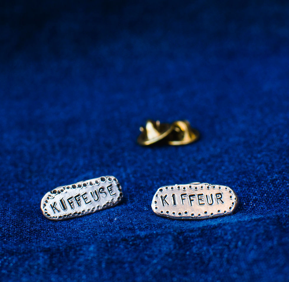 Pair of sterling silver pins with hand-stamped "Kiffeuse" and "Kiffeur", laid flat on blue fabric.