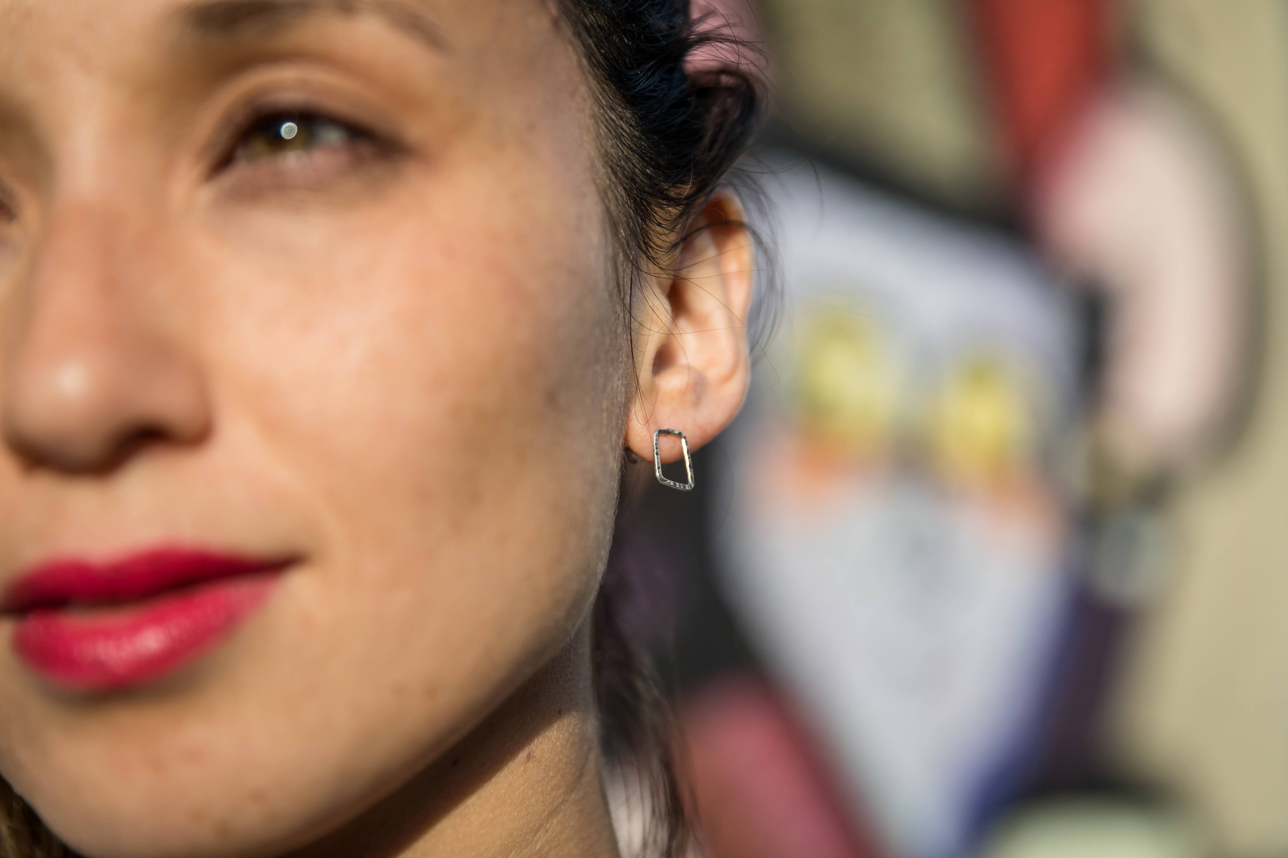 Close-up of a woman wearing a handmade sterling silver earring with a hammered finish. Geometric design.