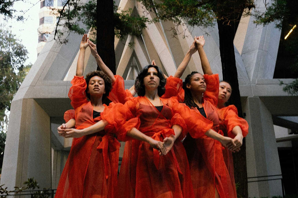 A star of dancers in bright, gauze orange costumes faces outwards, hands interconnecting in outward triangles.