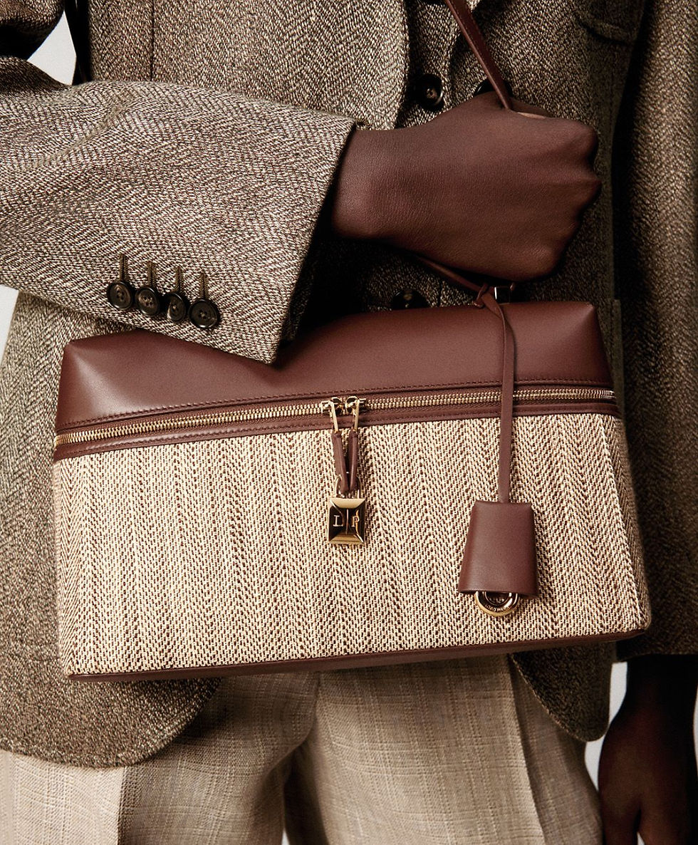 Person holding a brown and beige textured handbag, wearing a herringbone jacket. The setting is neutral, focusing on the fashion elements.