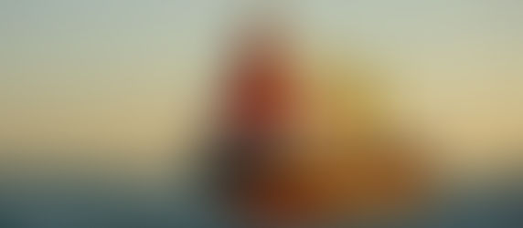 Navio cargueiro vermelho e branco com guindastes amarelos navega no mar ao pôr do sol. Texto: "PUFFIN S MONROVIA". Horizonte ao fundo.