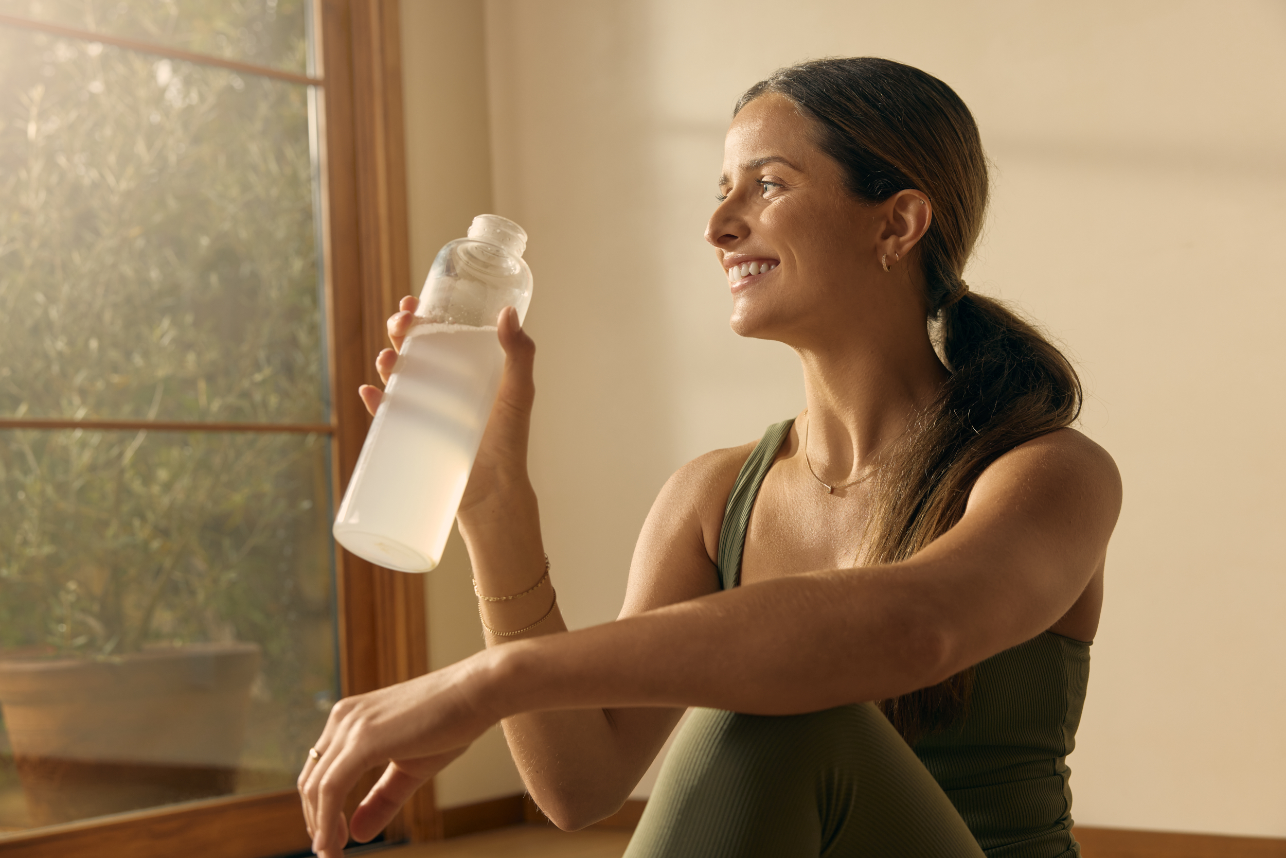 Woman holding a clear water bottle after mixing Goodonya Organic Electrolytes.