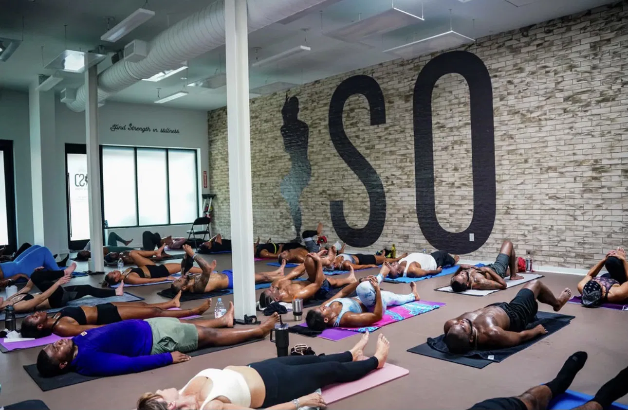 Yogis rest in savasana beneath large ISO logo inside bright studio at ISO Yoga Atlanta.