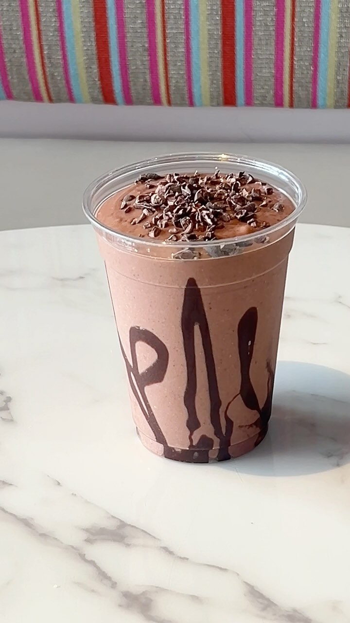 Thick chocolate smoothie in clear cup with chocolate drizzle rim.