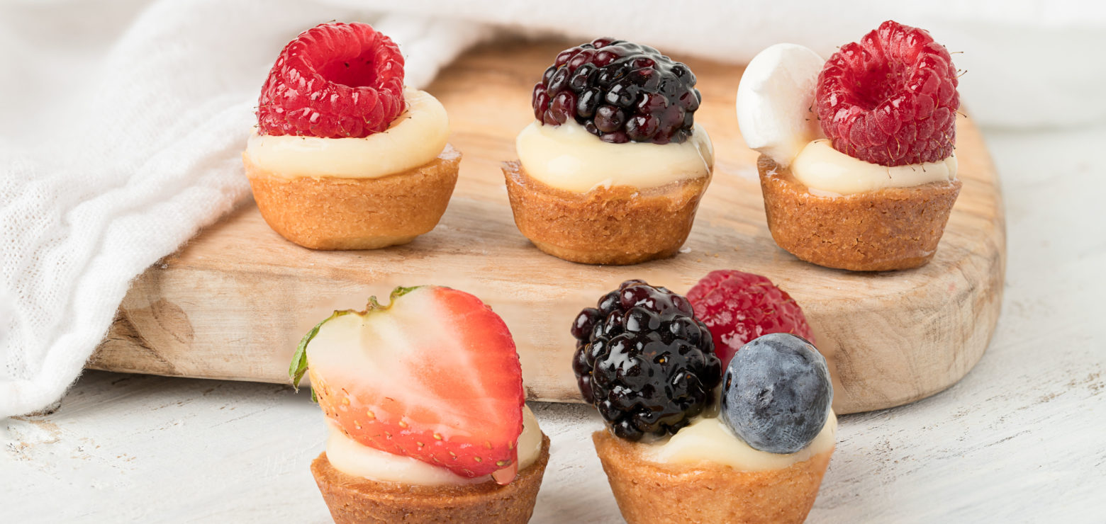 Small berry-topped fruit tartlets on wooden board.