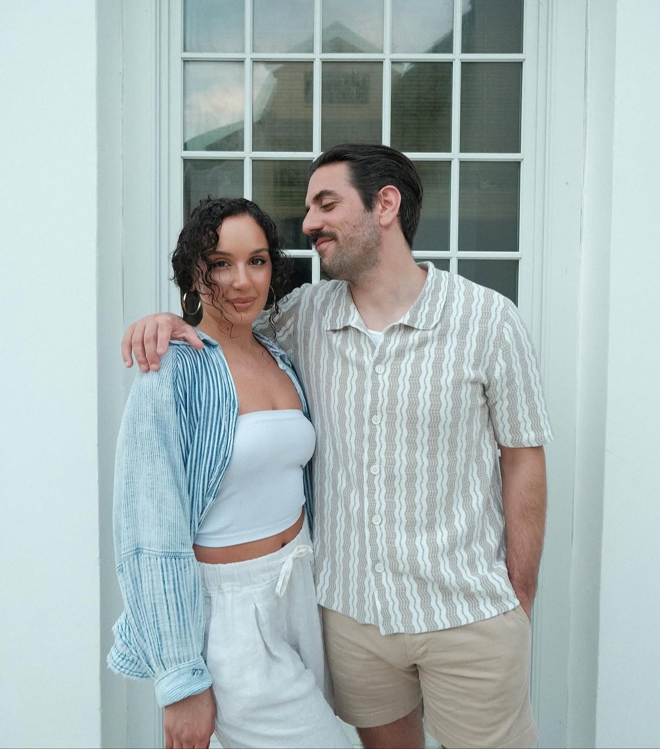 Casual couple by white door; natural, undetectable spray-tan finish – Muse Tan Atelier South End Charlotte