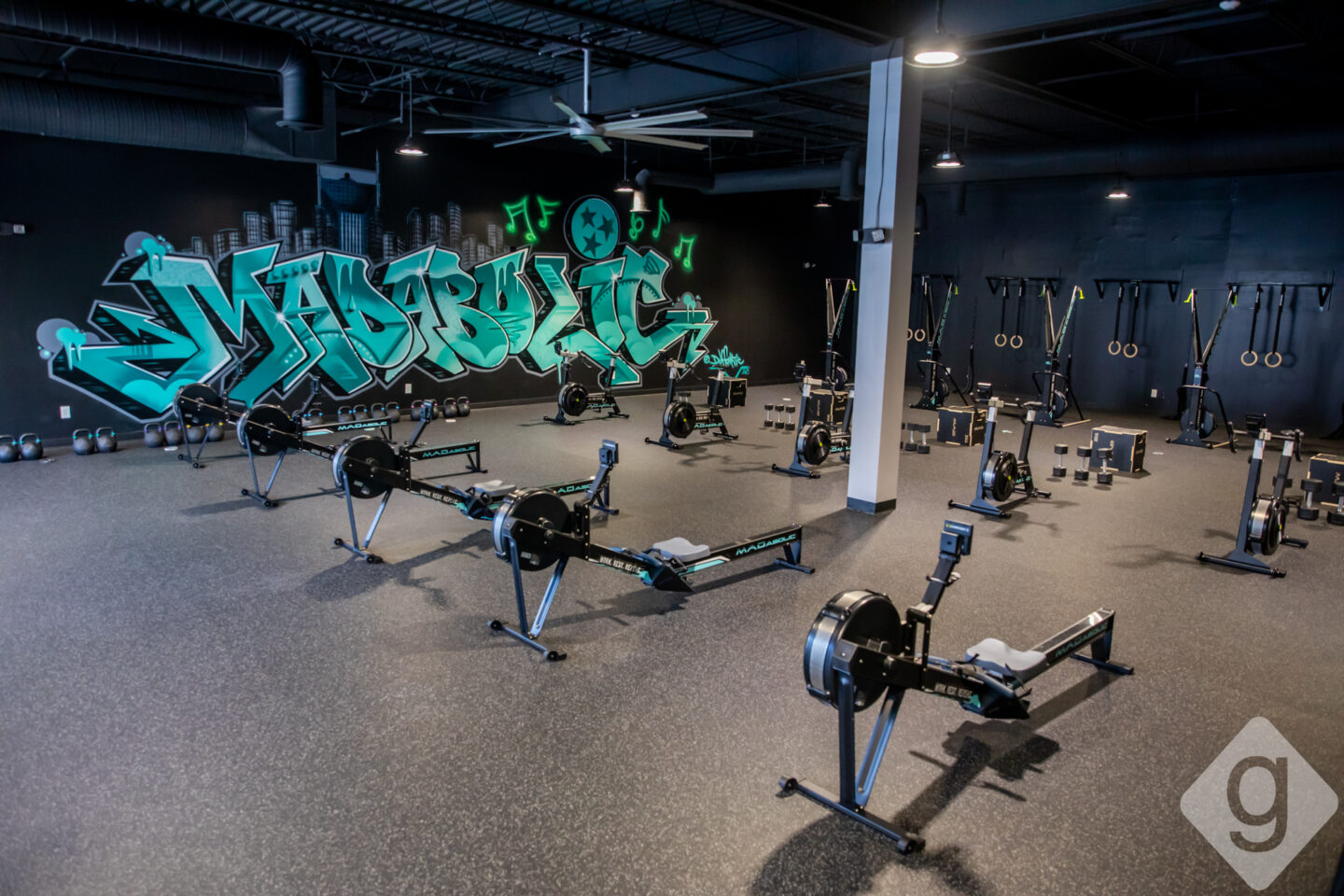 Empty MADabolic Atlanta floor featuring green graffiti wall, Concept2 rowers, turf lanes, and squat racks.