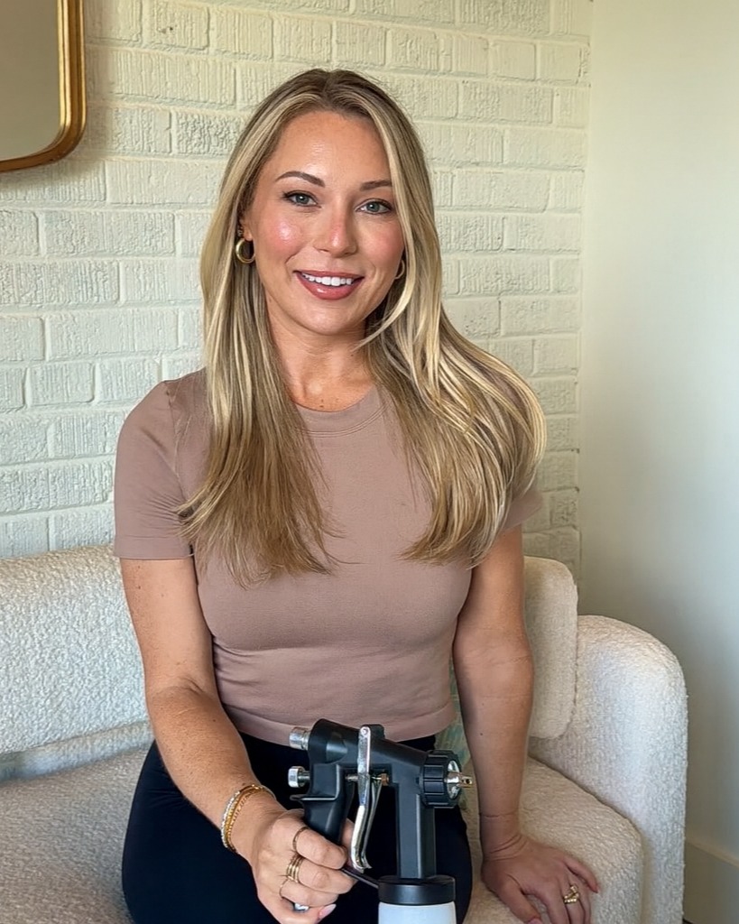 Woman seated indoors in neutral top, representing Sunless Glow by LA studio.