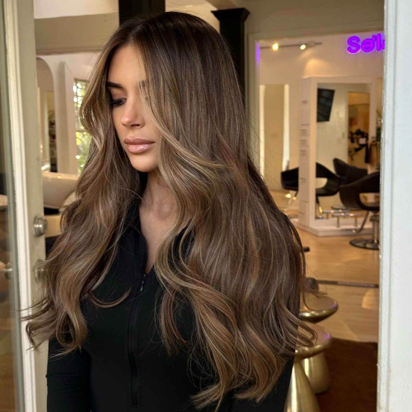 Voluminous brunette balayage curls on salon client in black top.