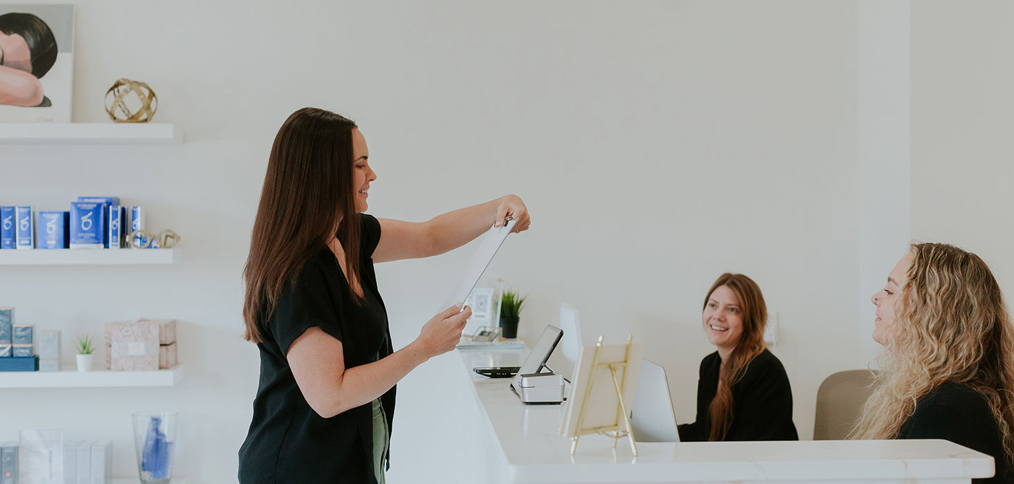 Staff member advising two clients at the reception counter.