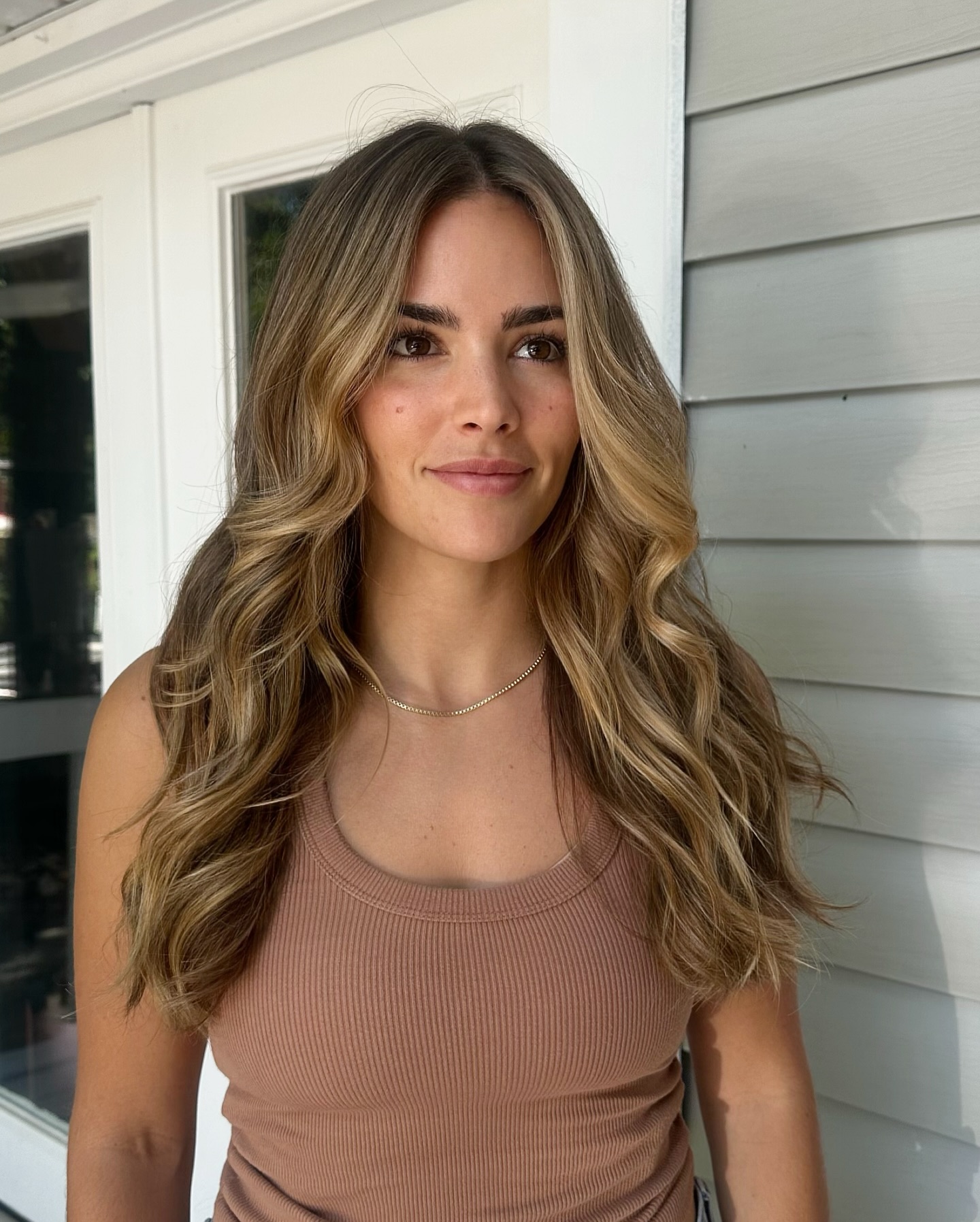 Soft honey-blonde balayage curls on woman outside Kayleigh Aesthetics.