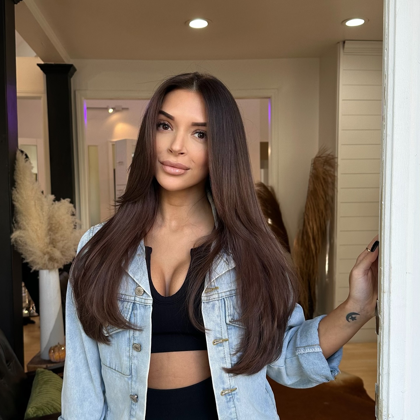 Straight chestnut-brown hair on woman in denim jacket at salon doorway.