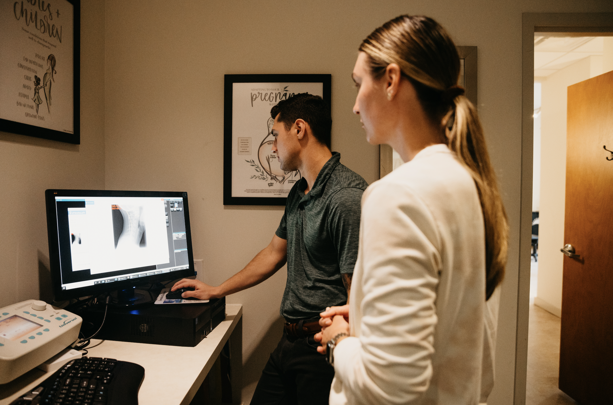 Chiropractor pointing to a spine x-ray on a monitor while speaking with a patient.