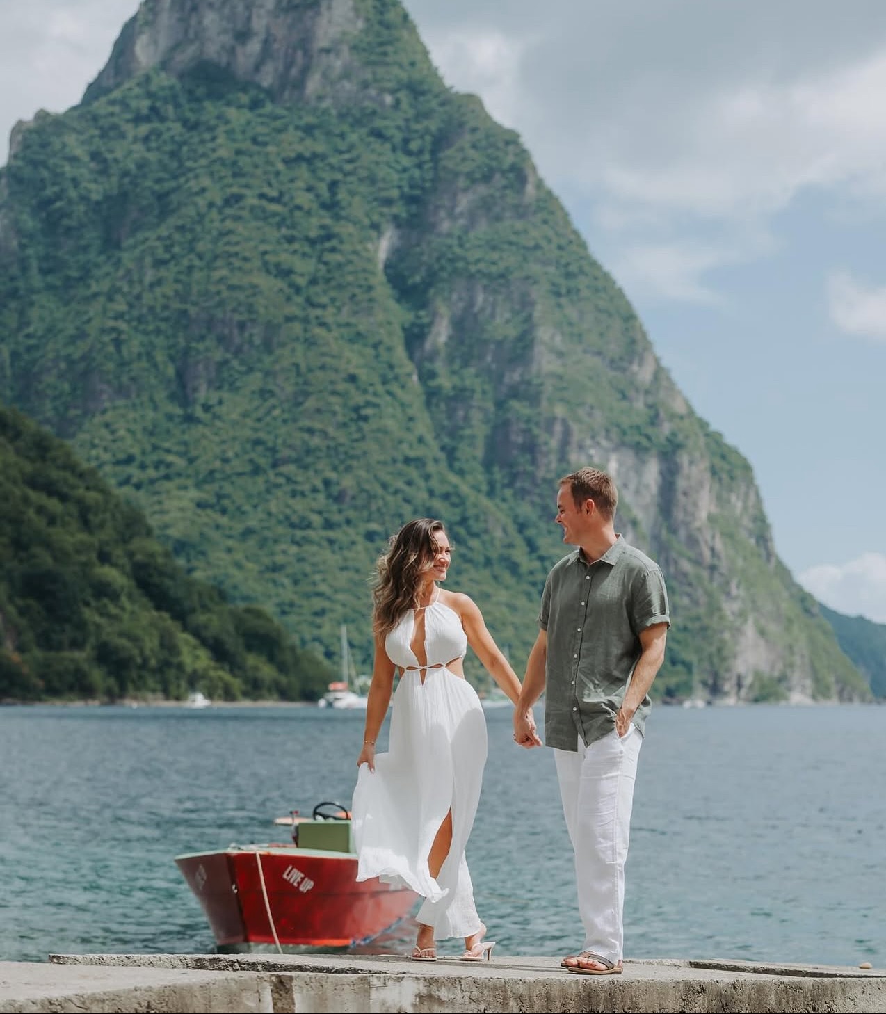 Couple on boat with mountain backdrop; woman in white dress with beachy glow – Muse Tan Atelier Charlotte
