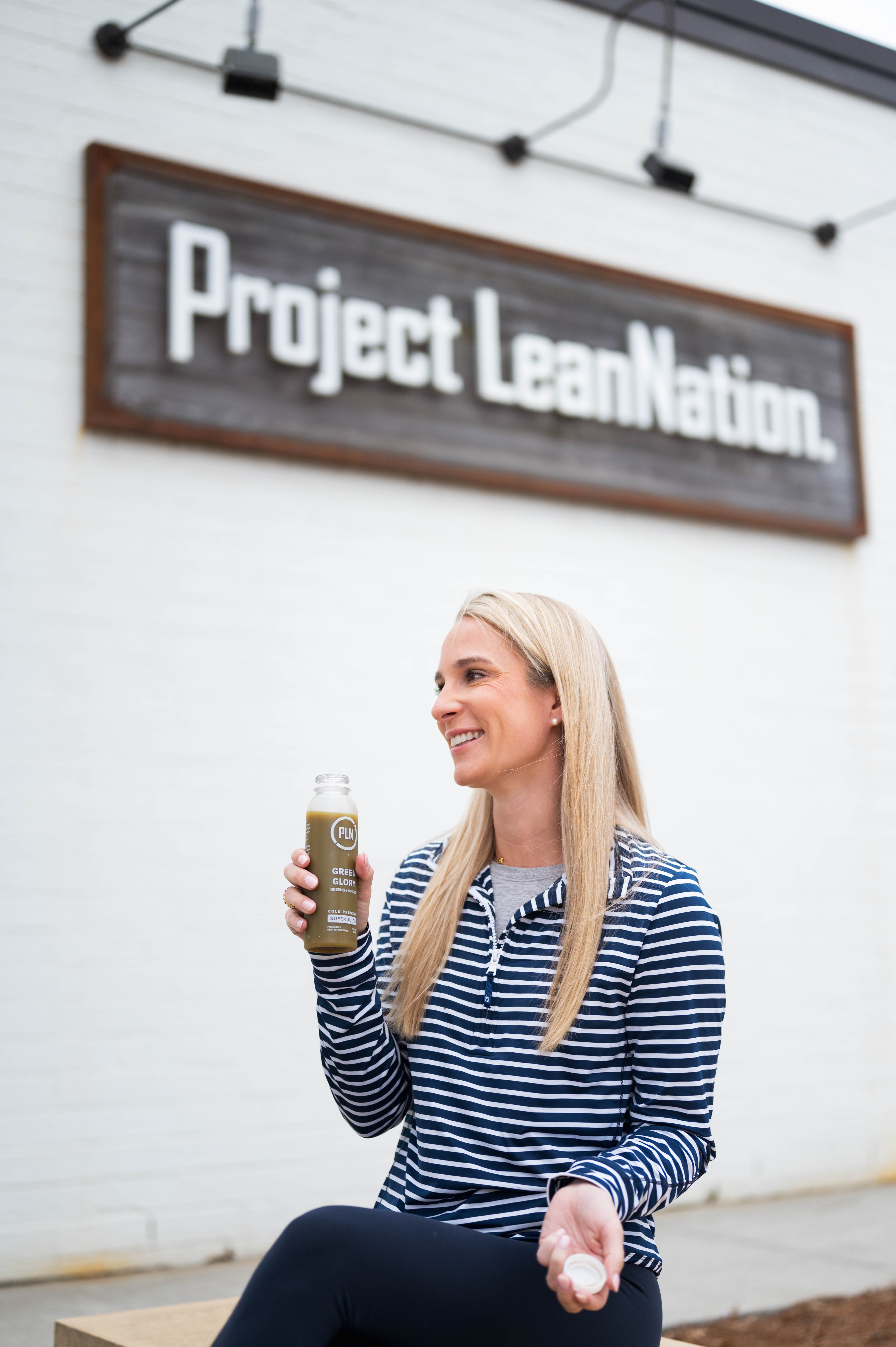 Person sitting outside with a Project LeanNation protein shake near the exterior sign in South End Charlotte.