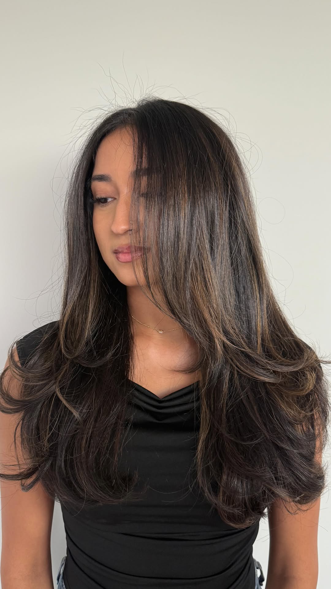 Woman with long brunette hair and face-framing layers in a shiny blowout.