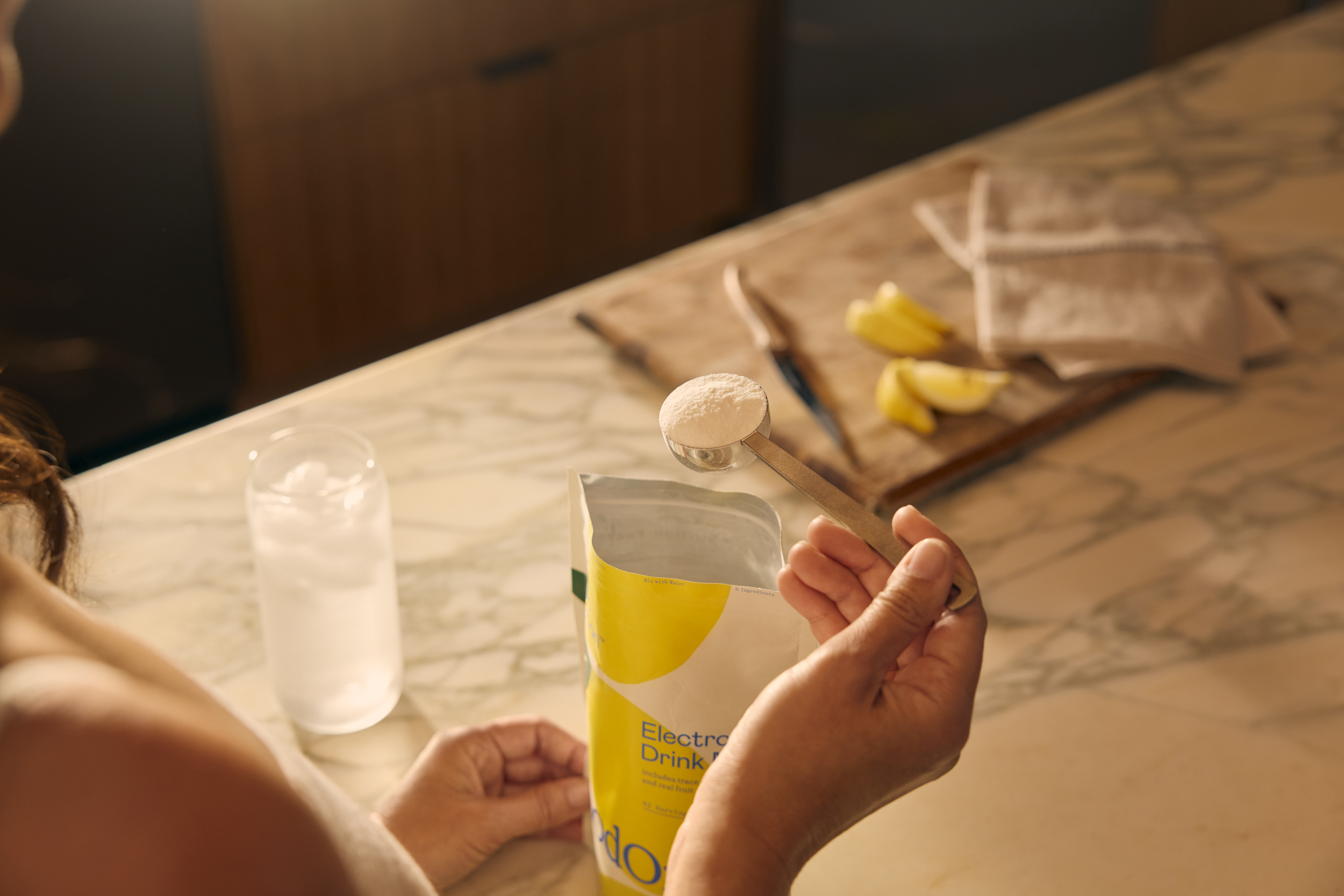 Hand stirring a jar next to a Goodonya canister and lemon wedge.