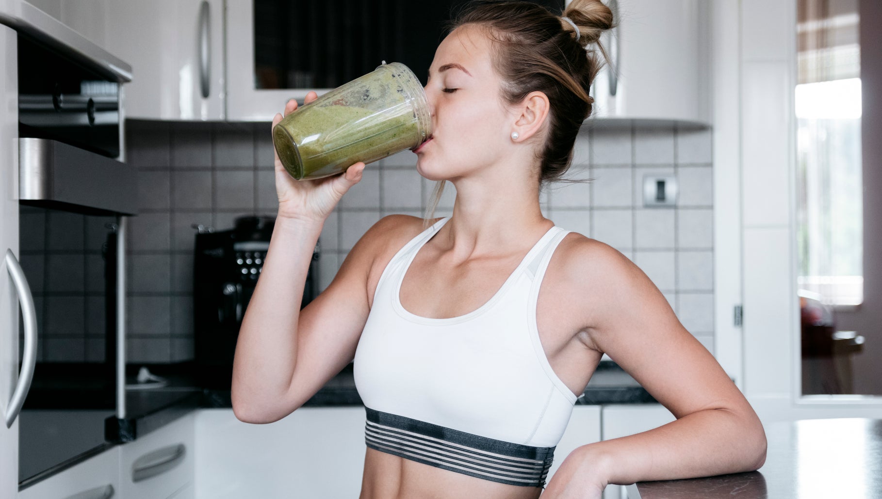 Woman in a bright kitchen drinking a green smoothie to support healthy weight loss habits