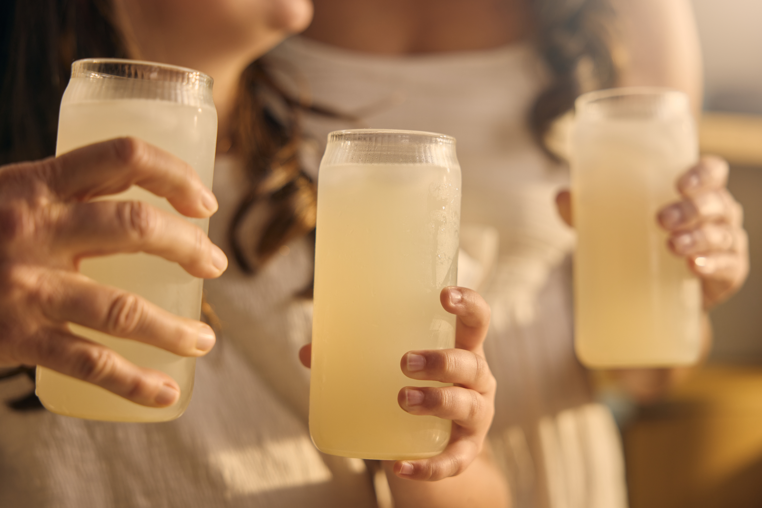 Three hands clinking mason jars of pale yellow Goodonya electrolyte drink.