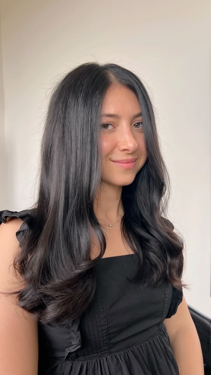 Woman with long dark hair styled in soft waves against a white background