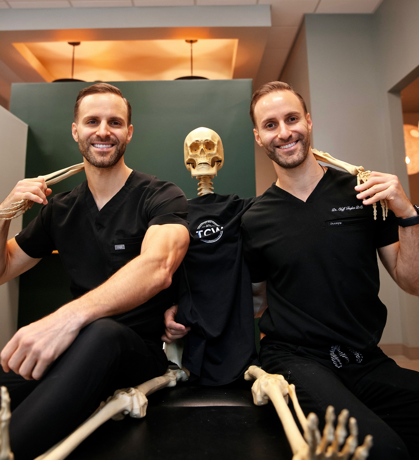 Two chiropractors with a skeleton model in an exam room.