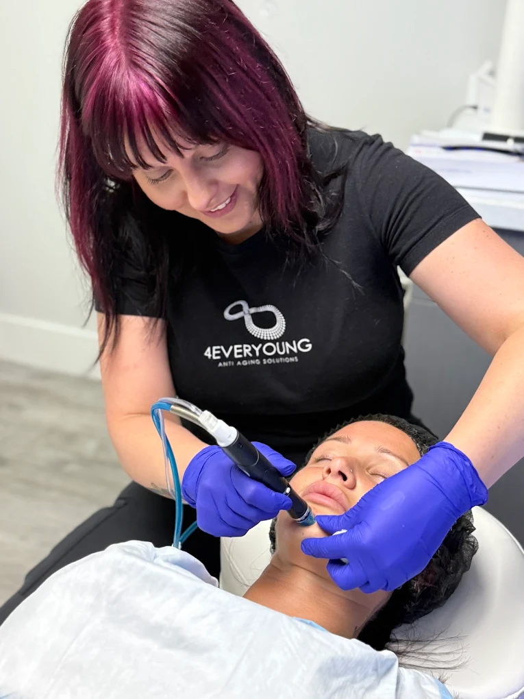 Provider in gloves using a handheld device on a client’s face during treatment.