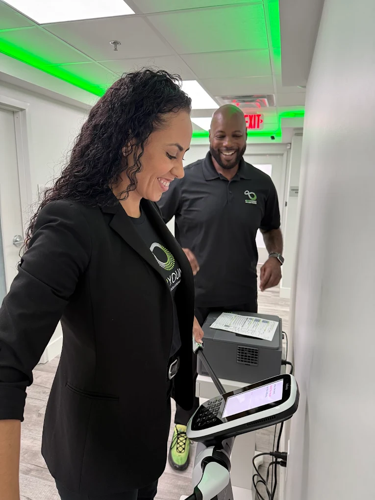 Staff member standing beside a medical aesthetic device in a bright hallway.