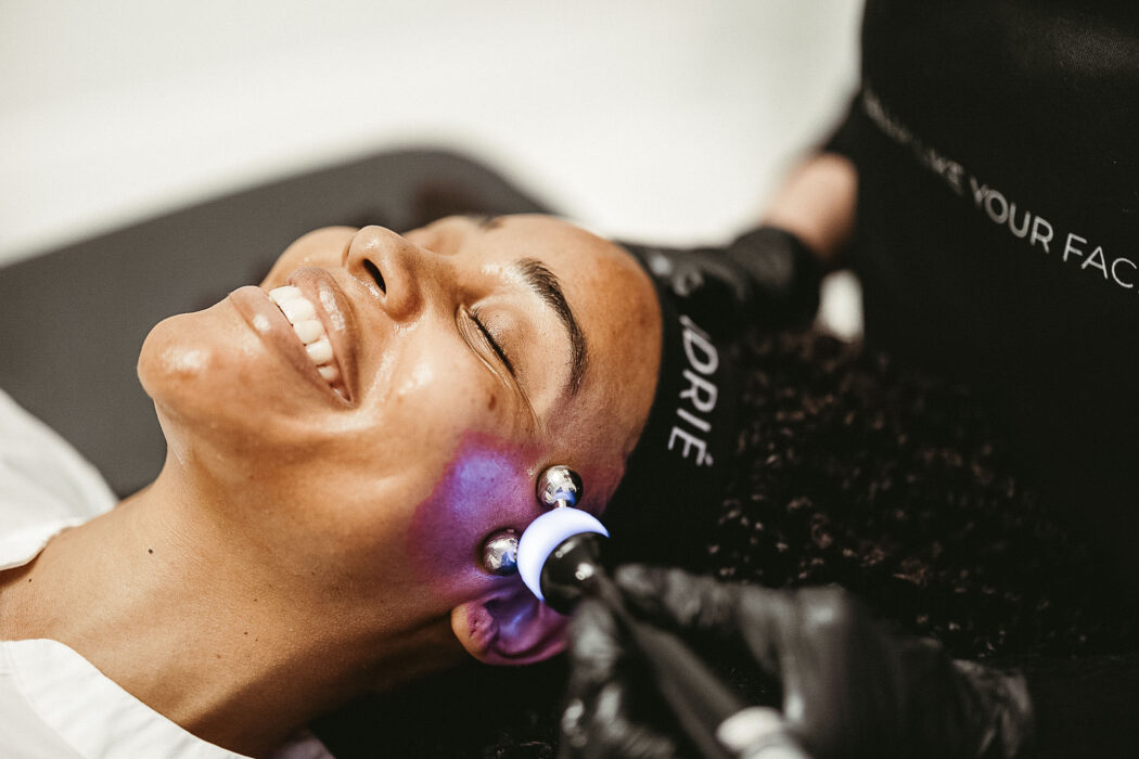 Woman smiling while esthetician rolls cooling globes across her cheeks at FACE FOUNDRIÉ Charleston – Mount Pleasant.