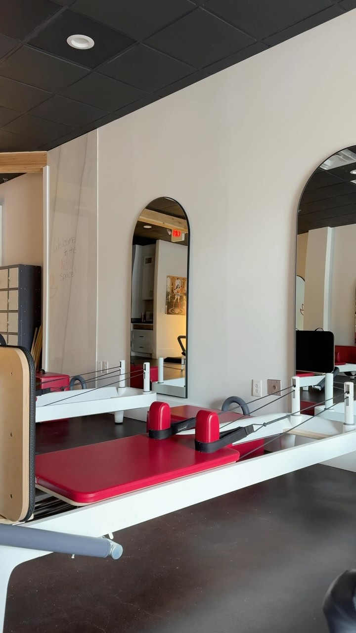 Row of red-upholstered reformers and mirrors at Naked Mind Studio Roswell Pilates room.