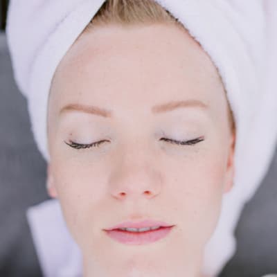 Woman with a towel head wrap resting with eyes closed after a facial.