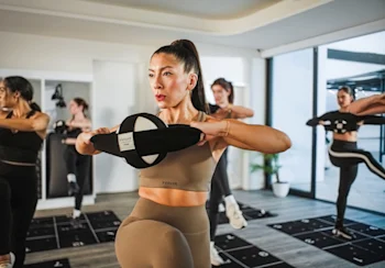 with smart programming, form cues, and equipment that target glutes, core, and hips.
Instructor in a tan workout set holding a Pvolve ring while coaching clients during class at Pvolve Krog Atlanta Beltline.