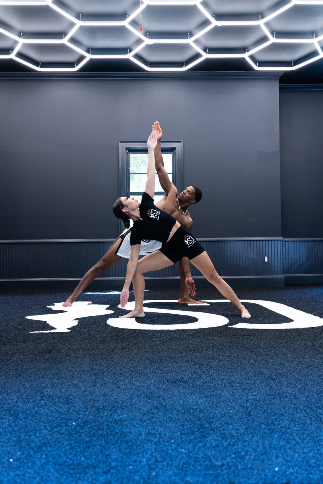 Trainer adjusts athlete in ISO Yoga Atlanta functional mobility session on blue mat.