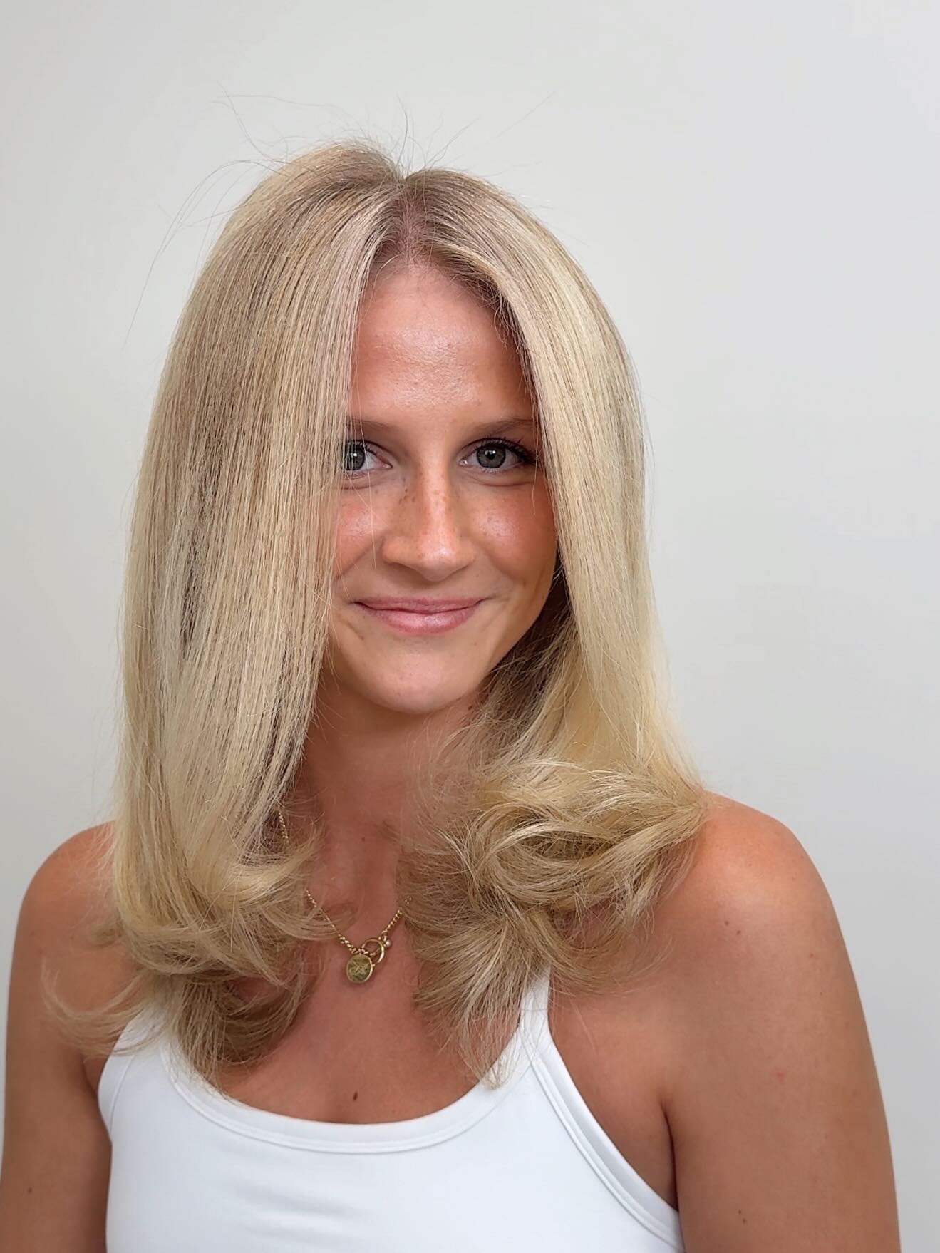 Smiling blonde client with layered haircut and voluminous blowout.
