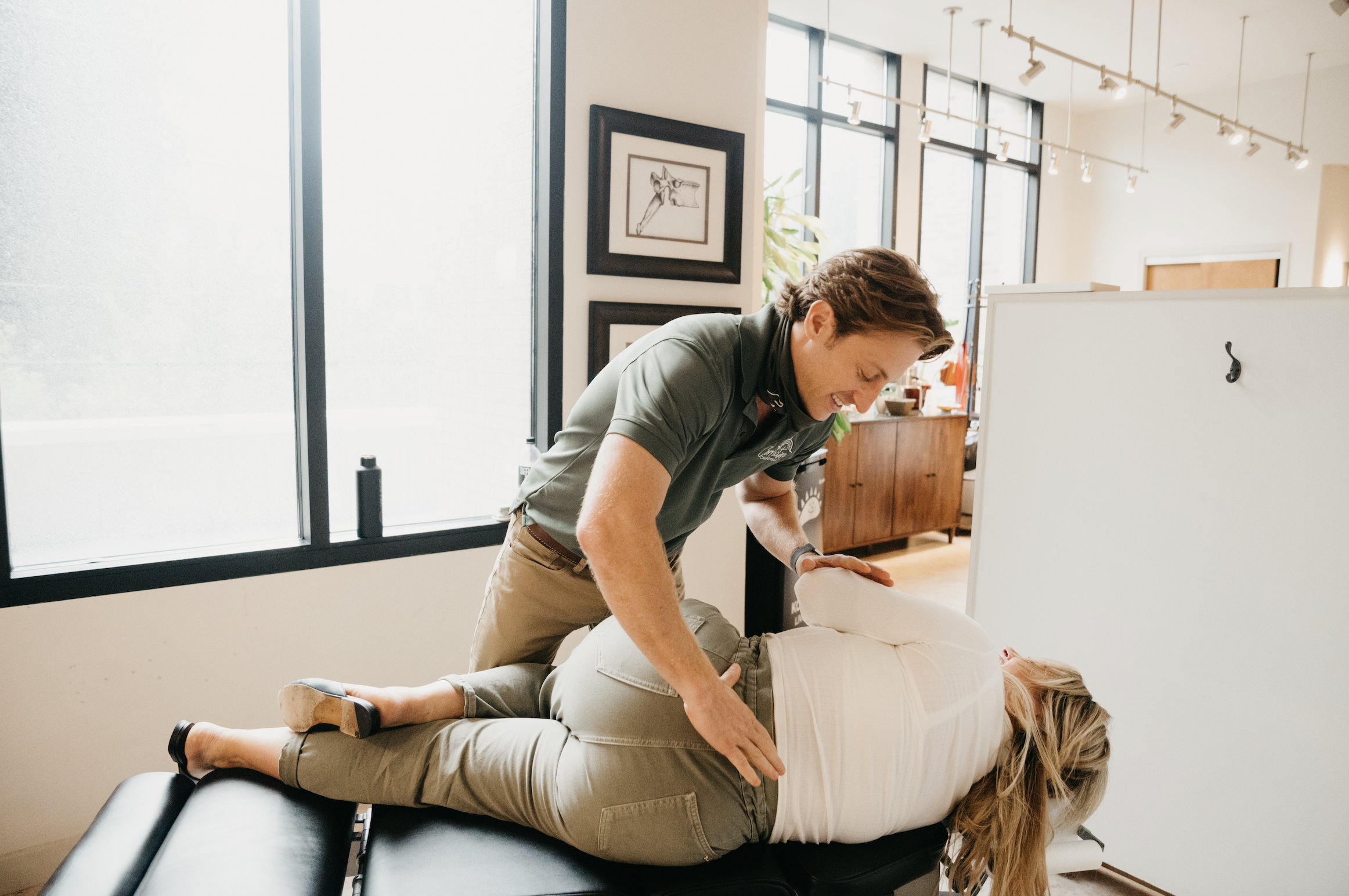 Pregnant woman lying on her side on an exam table while the chiropractor supports her hip during a prenatal adjustment.