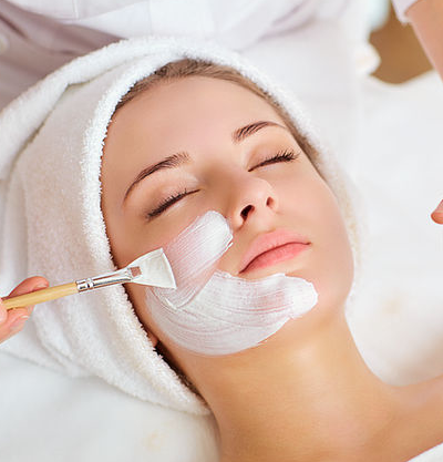 Esthetician brushing a white facial mask on a relaxed client.
