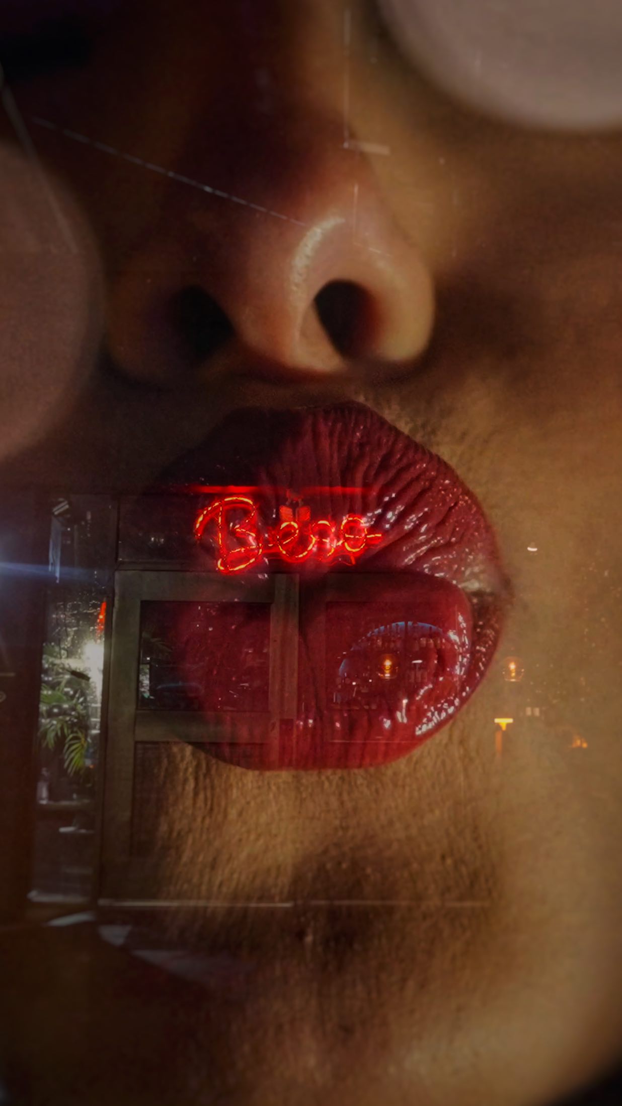 Close-up of glossy red lips with red “Beso” neon reflection.
